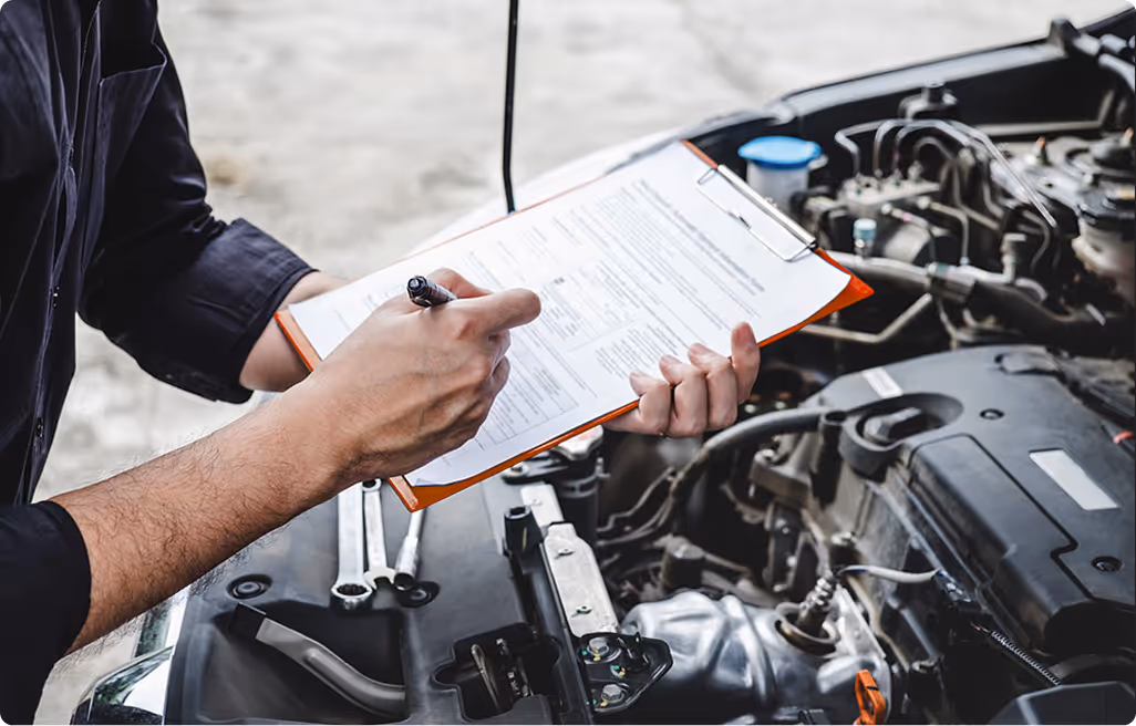 Person holding a clipboard and pen, inspecting and recording data on a checklist beside a car engine.