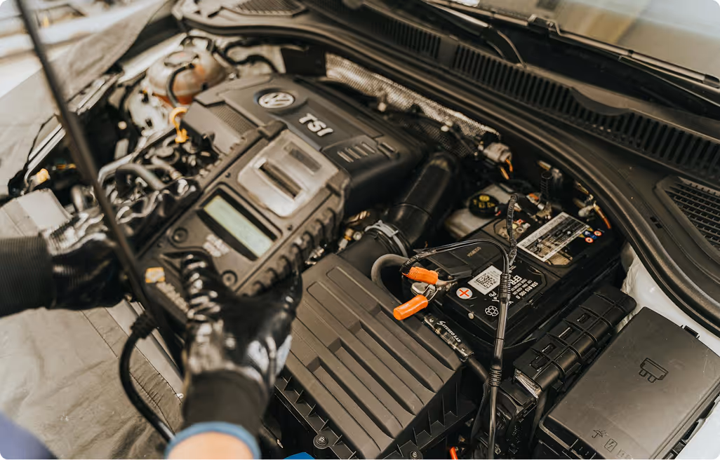 Technician wearing black gloves running a diagnostic tool on a Volkswagen TSI engine under a car hood.
