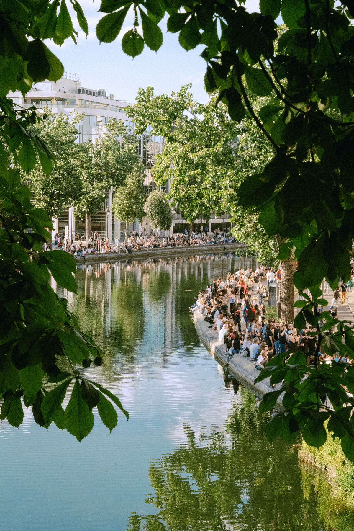 Berges ensoleillées du Canal Saint-Martin à Paris avec des passants profitant de l'extérieur. Vie de quartier parisienne avec Anchor.