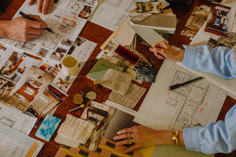 Deux personnes planifient un intérieur avec plans, échantillons de tissus et photos de décoration.