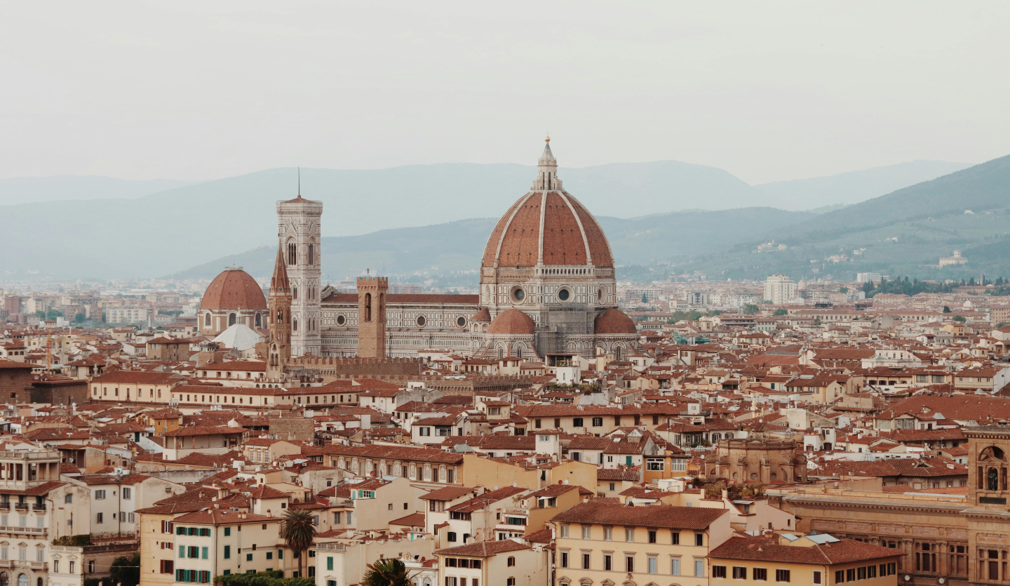 Vue de la cathédrale Santa Maria del Fiore à Florence avec ses toits rouges et les montagnes en arrière-plan.