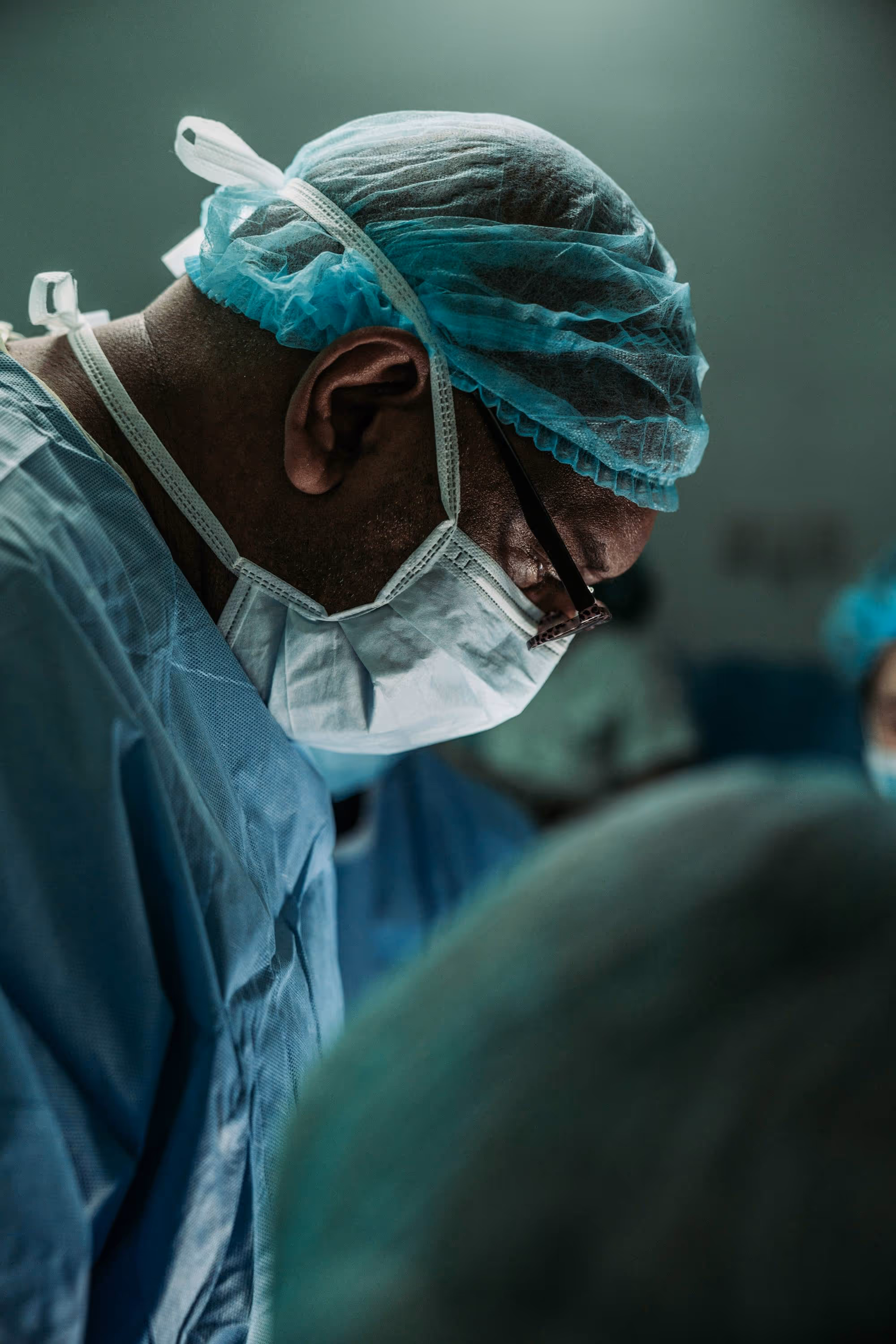 Surgeon wearing a surgical mask, cap, and gown focused during a medical procedure.