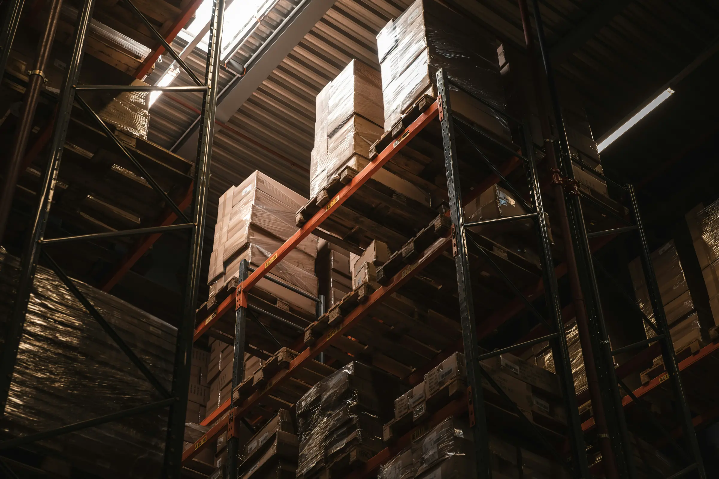 Warehouse shelves stacked with wrapped cardboard boxes under industrial lighting.