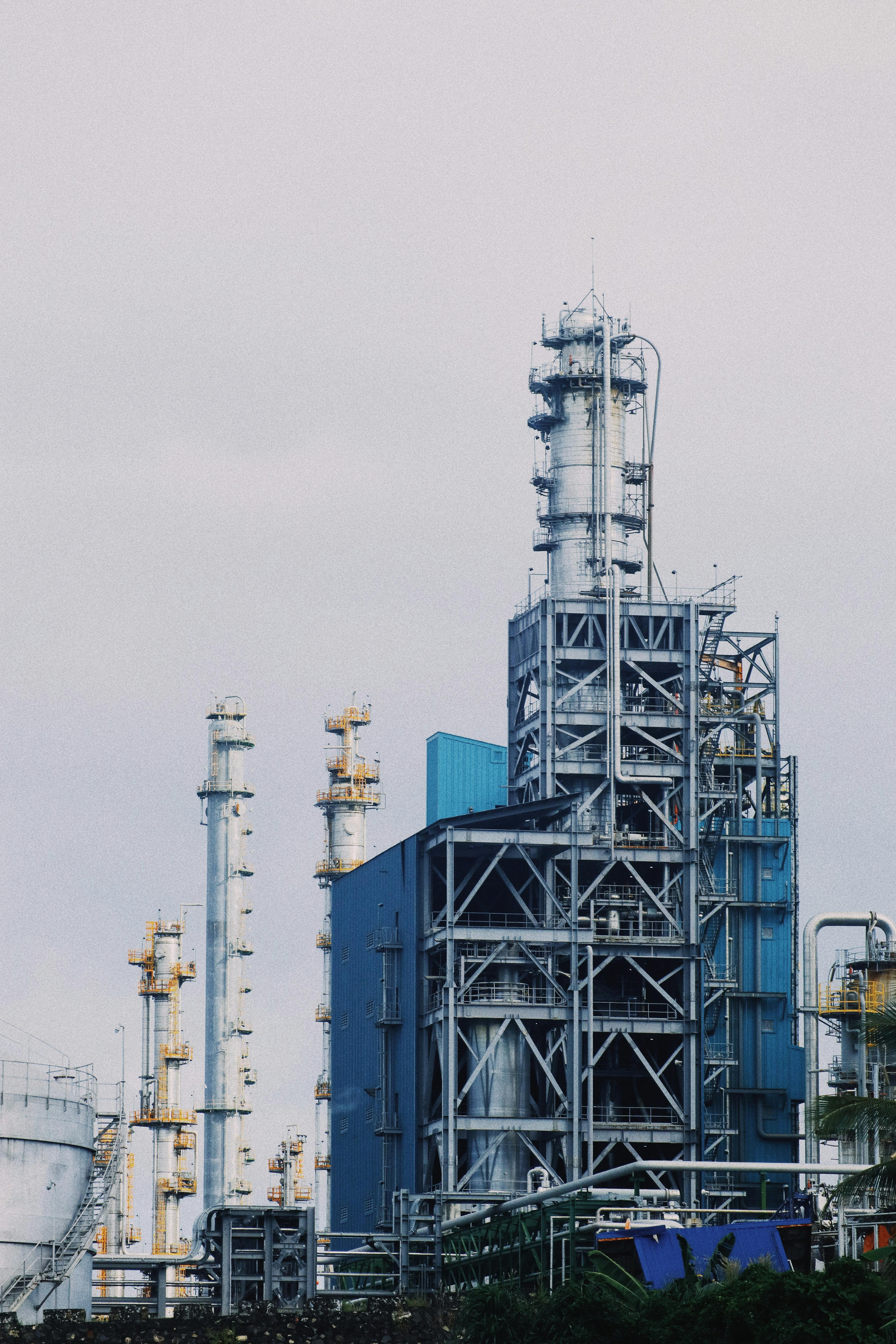 Industrial refinery plant with tall metal towers and structures under a cloudy sky.