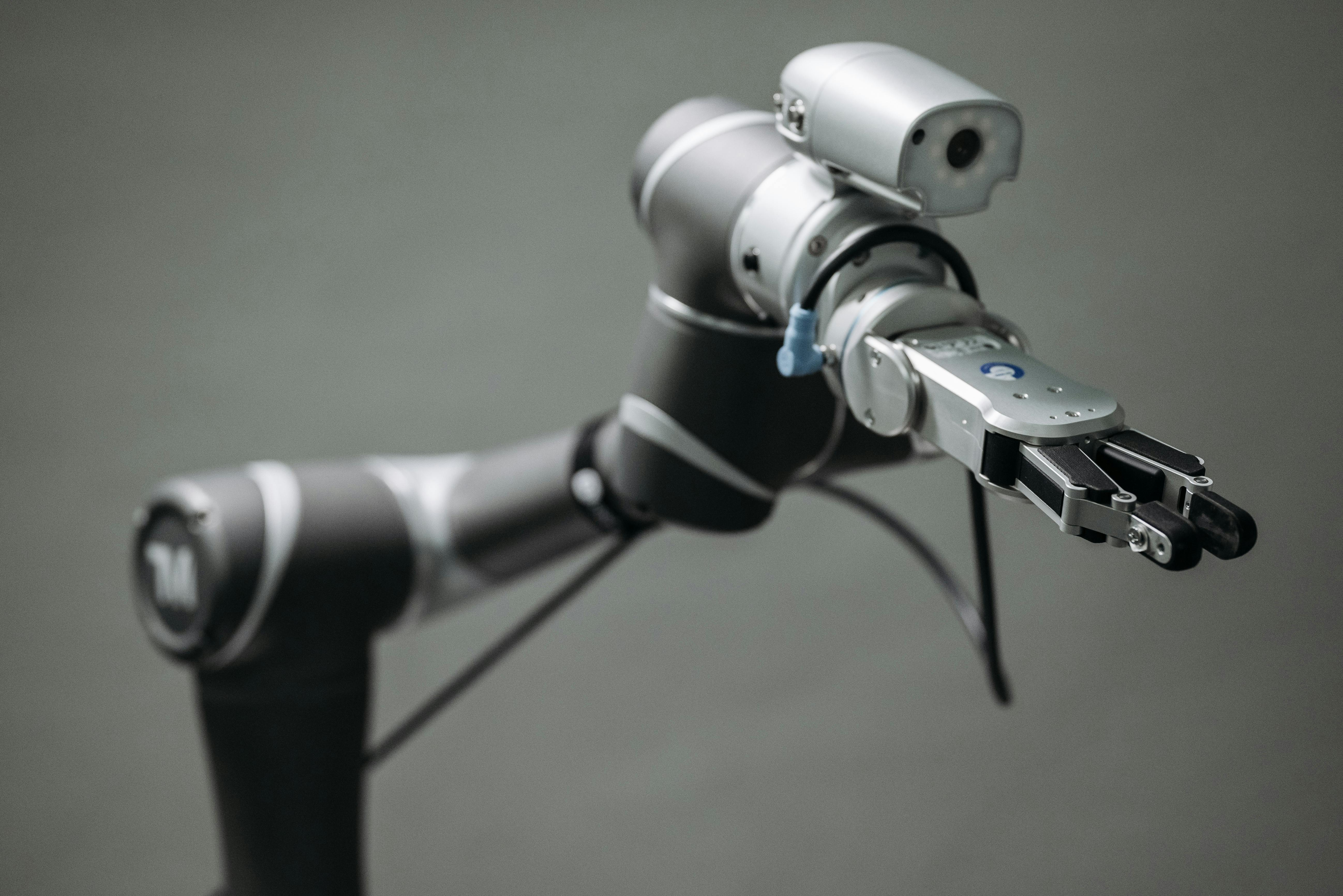 Close-up of a modern robotic arm with a gripper and attached sensor against a gray background.