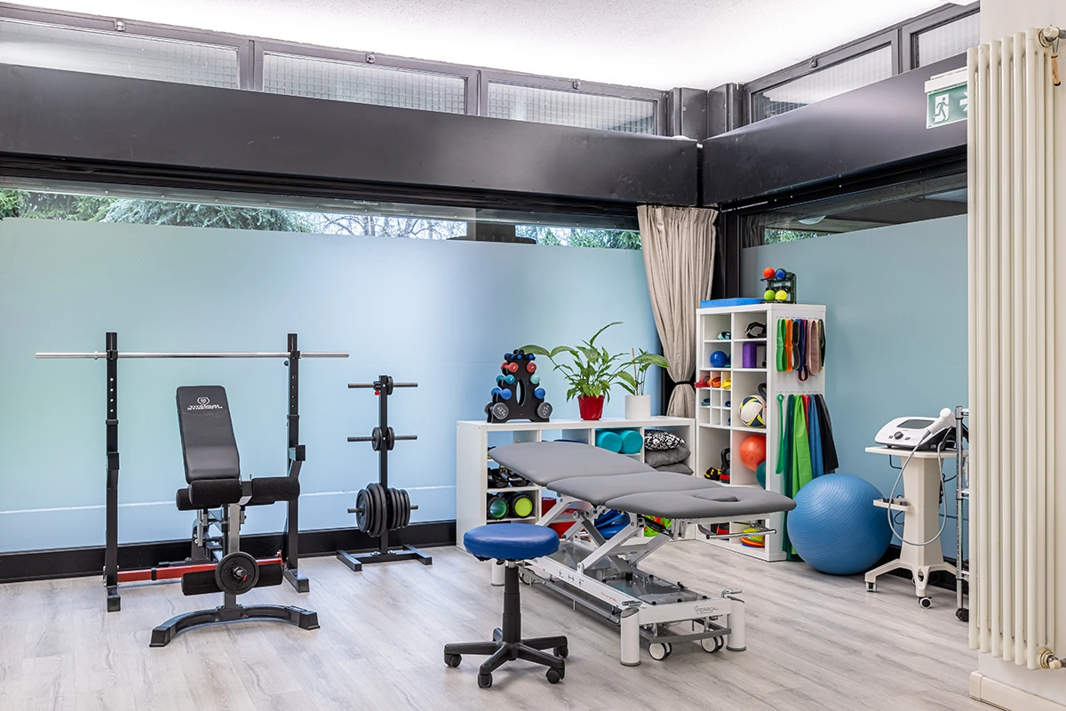 Studio fisioterapico moderno con panca per pesi, lettino da visita, pallone da ginnastica e vari attrezzi per riabilitazione.