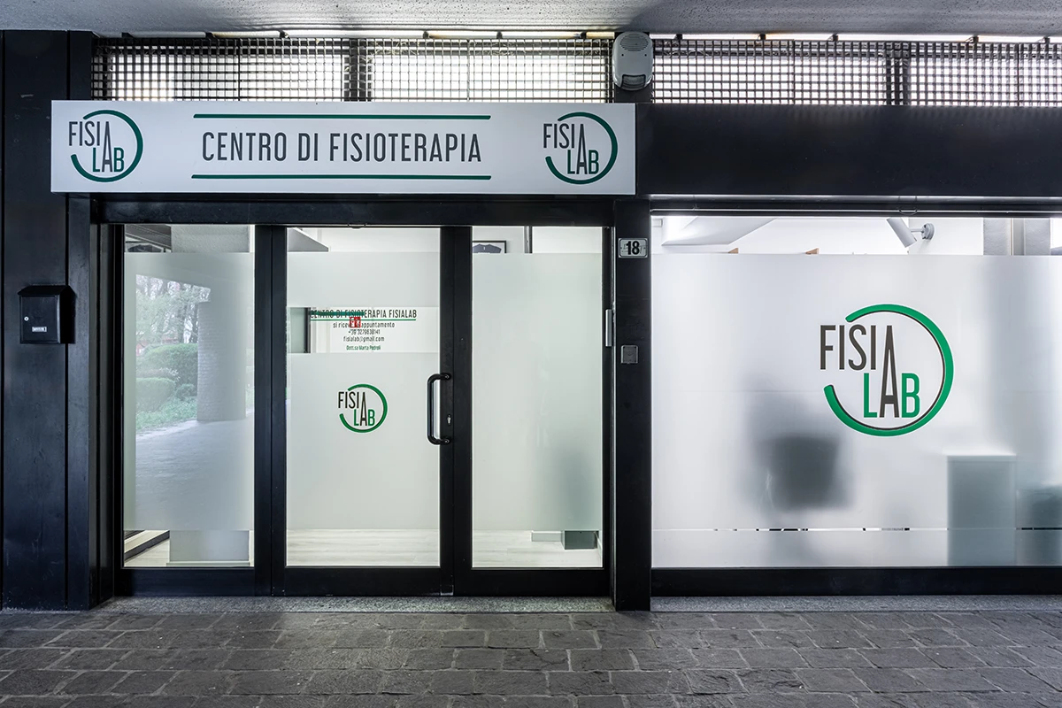 Ingresso moderno con vetrate opache di un centro di fisioterapia chiamato Fisialab, con insegna e logo ben visibili.