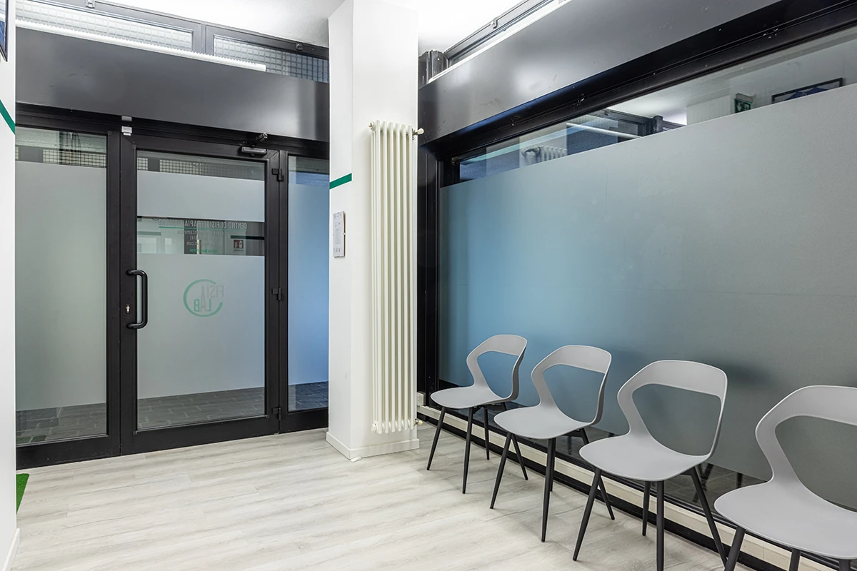 Sala d'attesa moderna con quattro sedie grigie e una porta di vetro scura.