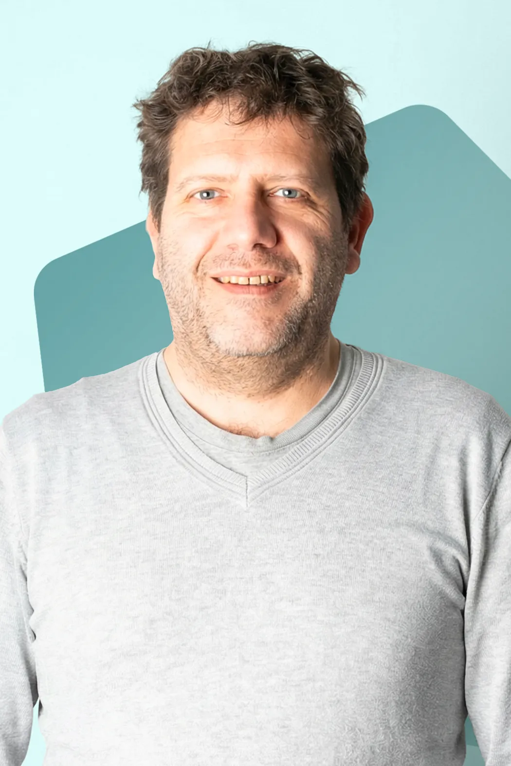 Smiling man with curly hair and beard wearing a light gray sweater against a blue background.