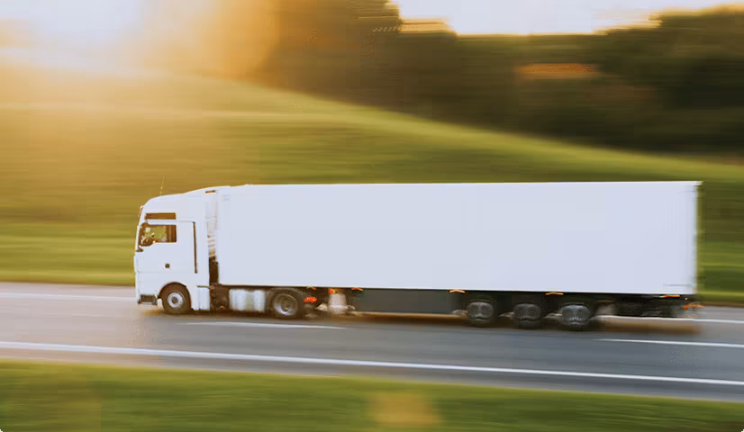 White semi-truck driving fast on a highway with blurred green landscape in the background during sunset.