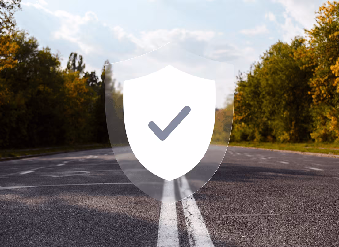 Een lege asfaltweg met een witte dubbele middenlijn en bomen langs de zijkanten, met een doorzichtige schild-icoon met een vinkje in het midden van de afbeelding.