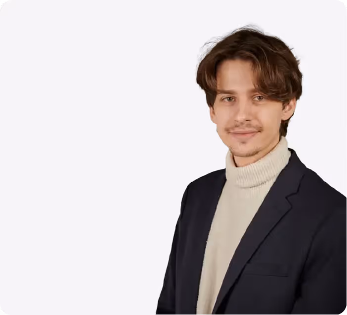 Porträt eines jungen Mannes mit braunen Haaren, der einen hellen Rollkragenpullover und ein dunkles Sakko trägt, vor weißem Hintergrund.