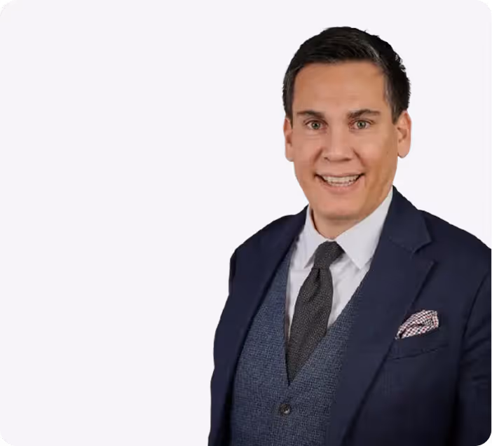 Lächelnder Mann mit dunklen Haaren in Anzug, Hemd und Krawatte vor weißem Hintergrund.