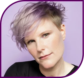 Das Portraitfoto zeigt eine weiße Person mit kurzen, hell-violett gefärbten und rot-blonden Haaren. Die Person ist weiß, hat den Kopf leicht nach links geneigt und guckt freundlich geradeaus in die Kamera. Die Person trägt ein schwarzes Shirt. Der Hintergrund ist hellviolett – ähnlich der Haarfarbe. Die abgebildete Person ist Daniela Schubert.
