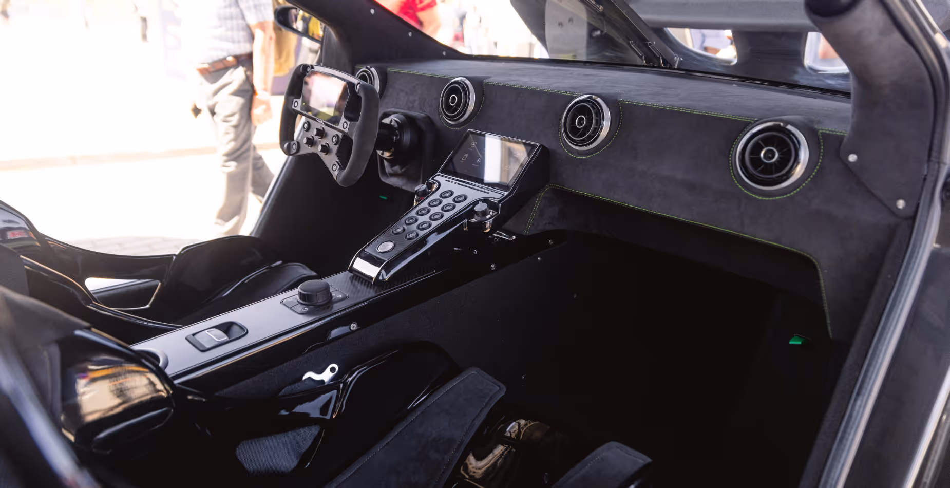 Interior of a modern car with a racing-style steering wheel, digital control panel, and sporty black seats.