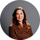 Woman with long brown hair wearing a brown checkered shirt against a gray background.