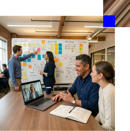 Four colleagues collaborating in a modern office with a whiteboard covered in sticky notes, discussing and video conferencing on a laptop.