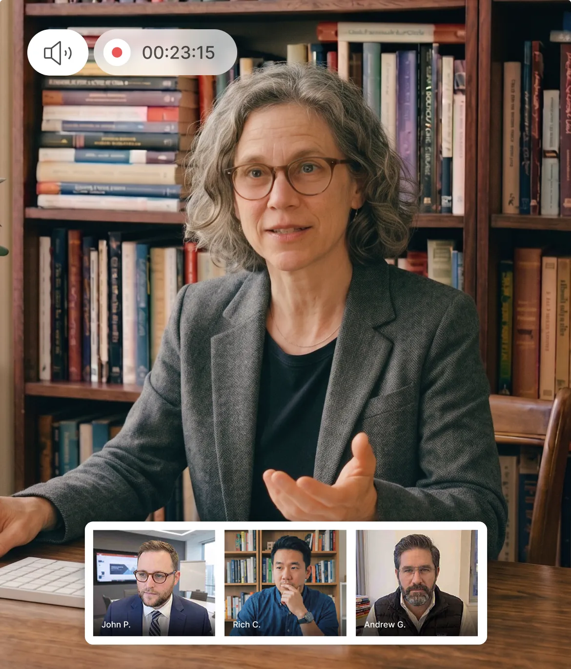 Woman with glasses and gray hair speaking in a video call with three men shown in smaller windows below her, surrounded by bookshelves.