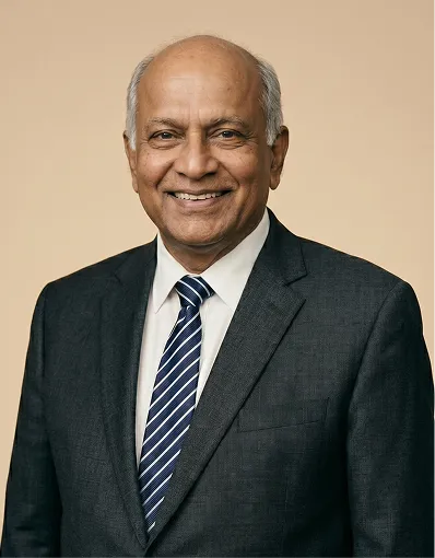 Smiling elderly man wearing a dark suit and blue striped tie against a neutral background.