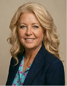 Smiling middle-aged woman with blonde hair, wearing a dark blazer and a blue floral blouse.