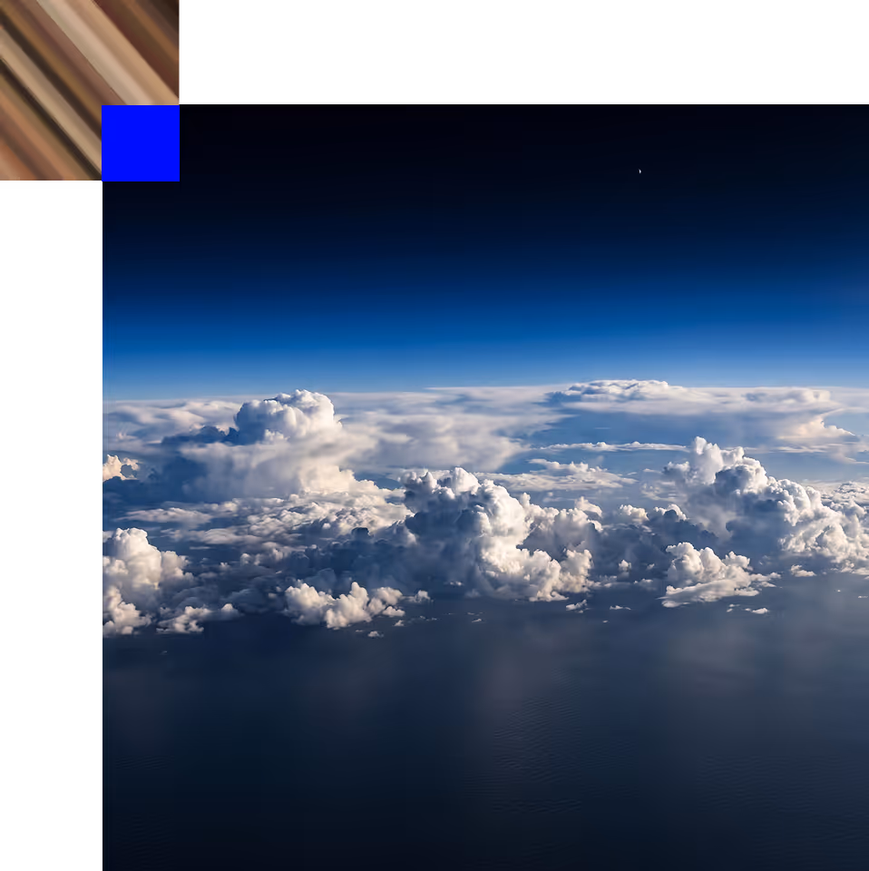 Fluffy white clouds over a calm dark ocean under a deep blue sky with a small crescent moon visible.