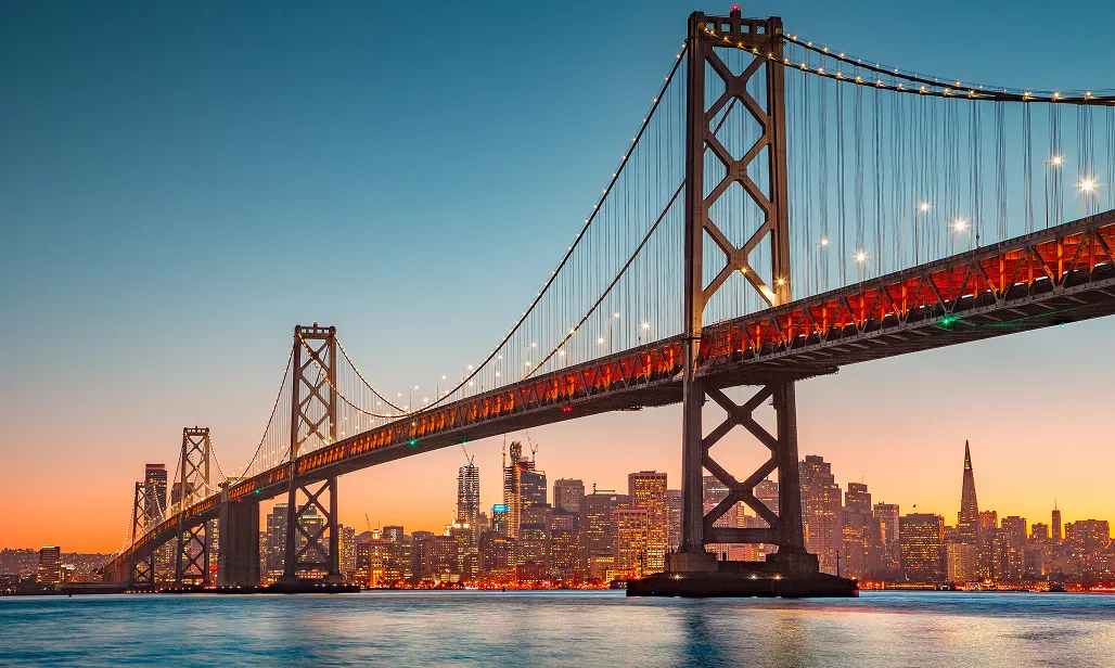 San Francisco city skyline with the illuminated Bay Bridge at sunset.
