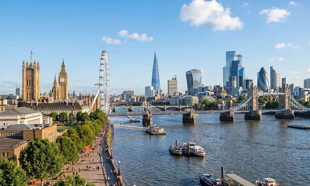 View of the London skyline featuring the Houses of Parliament, Big Ben, the London Eye, the Shard, Tower Bridge, and the River Thames on a partly cloudy day.