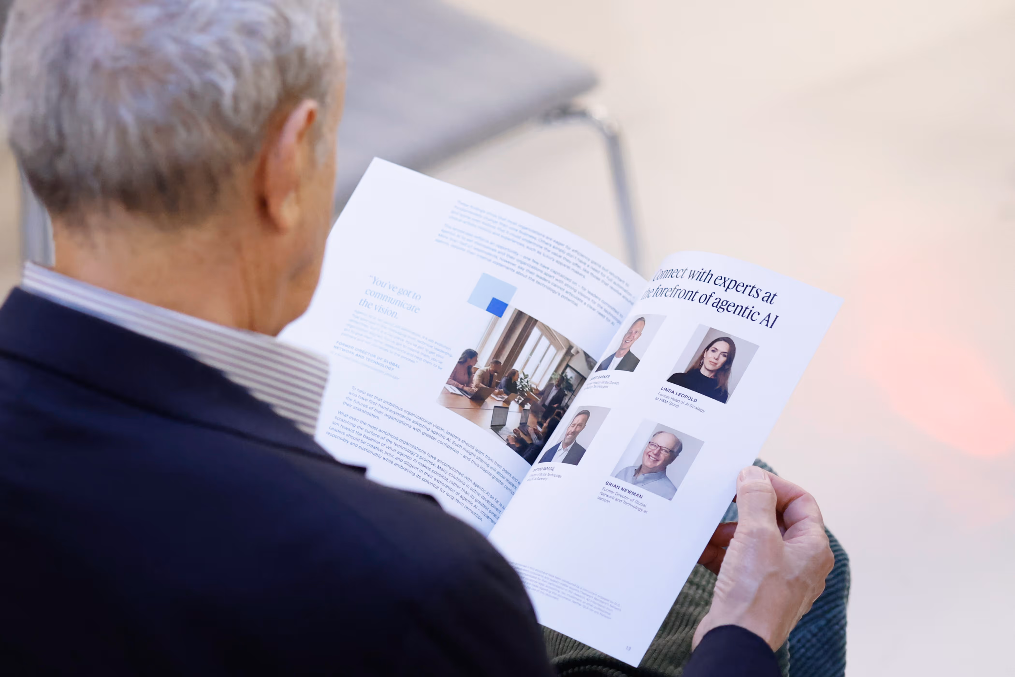 Older man in a dark jacket reading a brochure featuring experts in agentic AI and a group meeting photo.