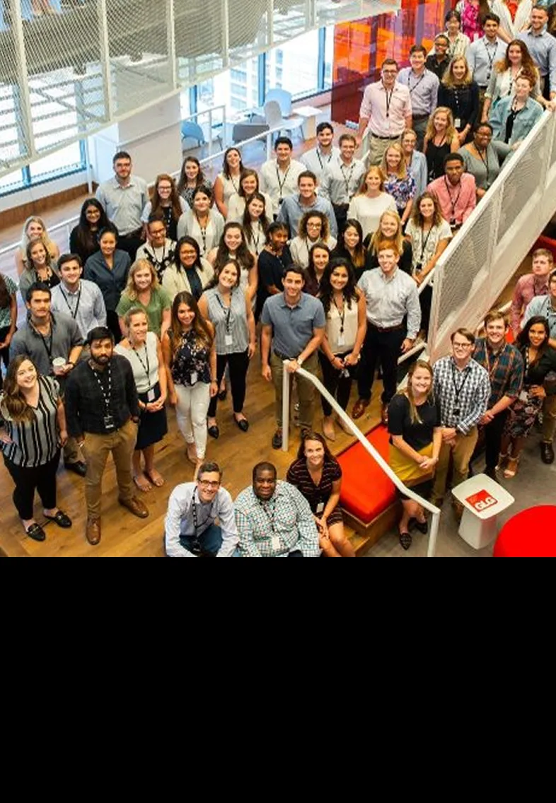 Large diverse group of people posing for a photo inside a modern office with wooden floors and red accents.