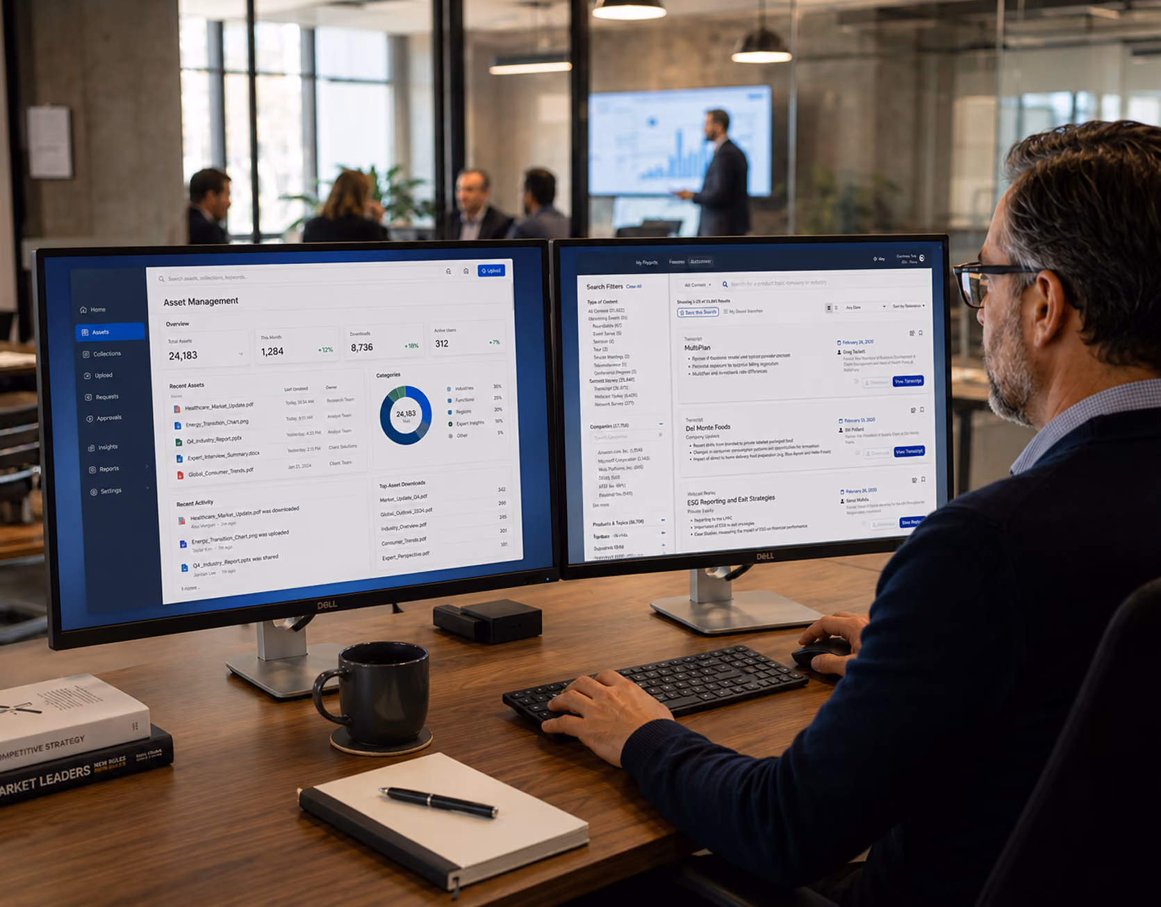 Man at desk using dual monitors displaying asset management and project data dashboards in office.