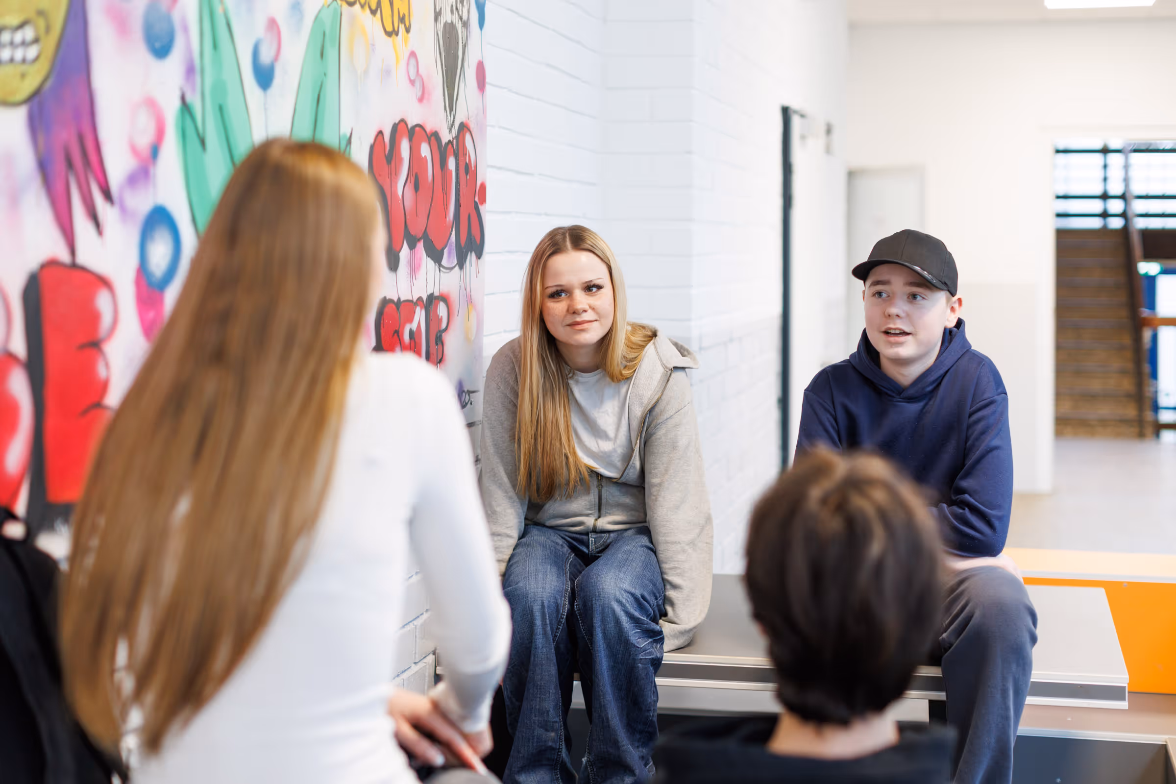 Mädchen in einem Klassenzimmer schreibt konzentriert mit einem Stift, zwei weitere Kinder sitzen im Hintergrund.