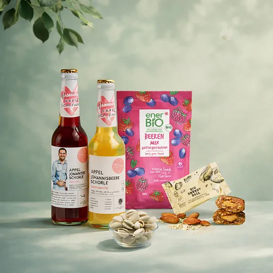 Zwei Flaschen Apfel-Johannisbeer Schorle, energetischer Beeremix und Snacks mit Nüssen und Samen auf hellem Hintergrund.