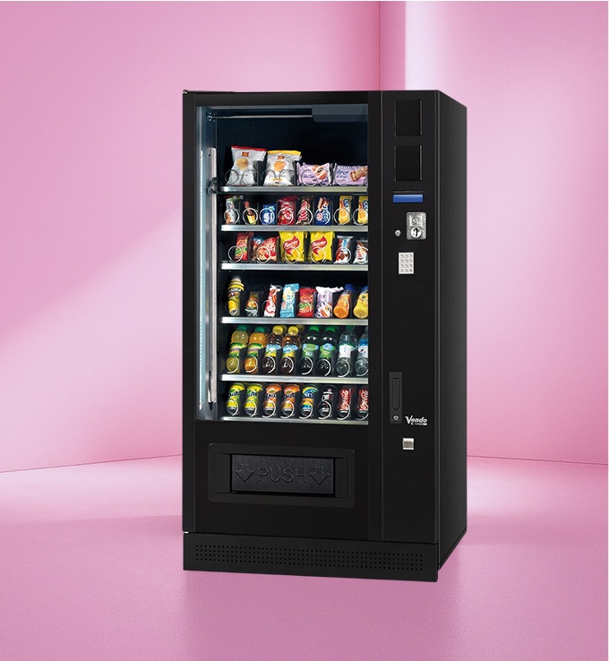 Schwarzer Snack- und Getränkeautomat vor pinker Wand mit verschiedenen Getränken und Snacks.