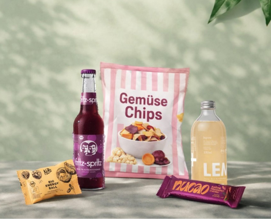 Nachhaltige Snacks mit Getränk, Gemüsechips und Energieriegel vor grünem Hintergrund