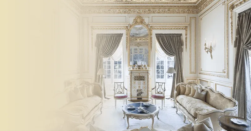 “Elegant drawing room with gilded plasterwork, tall sash windows, silk drapes, and antique sofas around a decorative fireplace.”