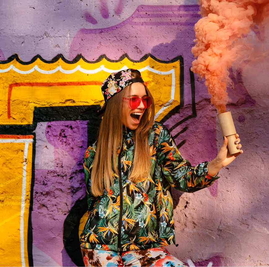 Trendy young woman posing with a smoke flare in front of a yellow and purple graffiti wall in Shoreditch.
