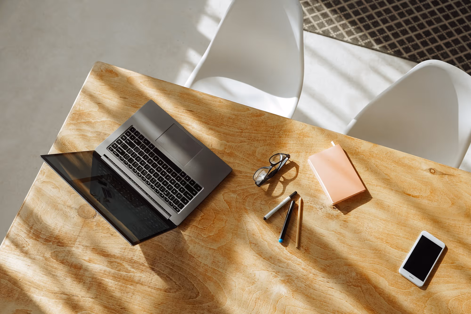 Laptop workspace on wooden desk with notebook and phone in natural light