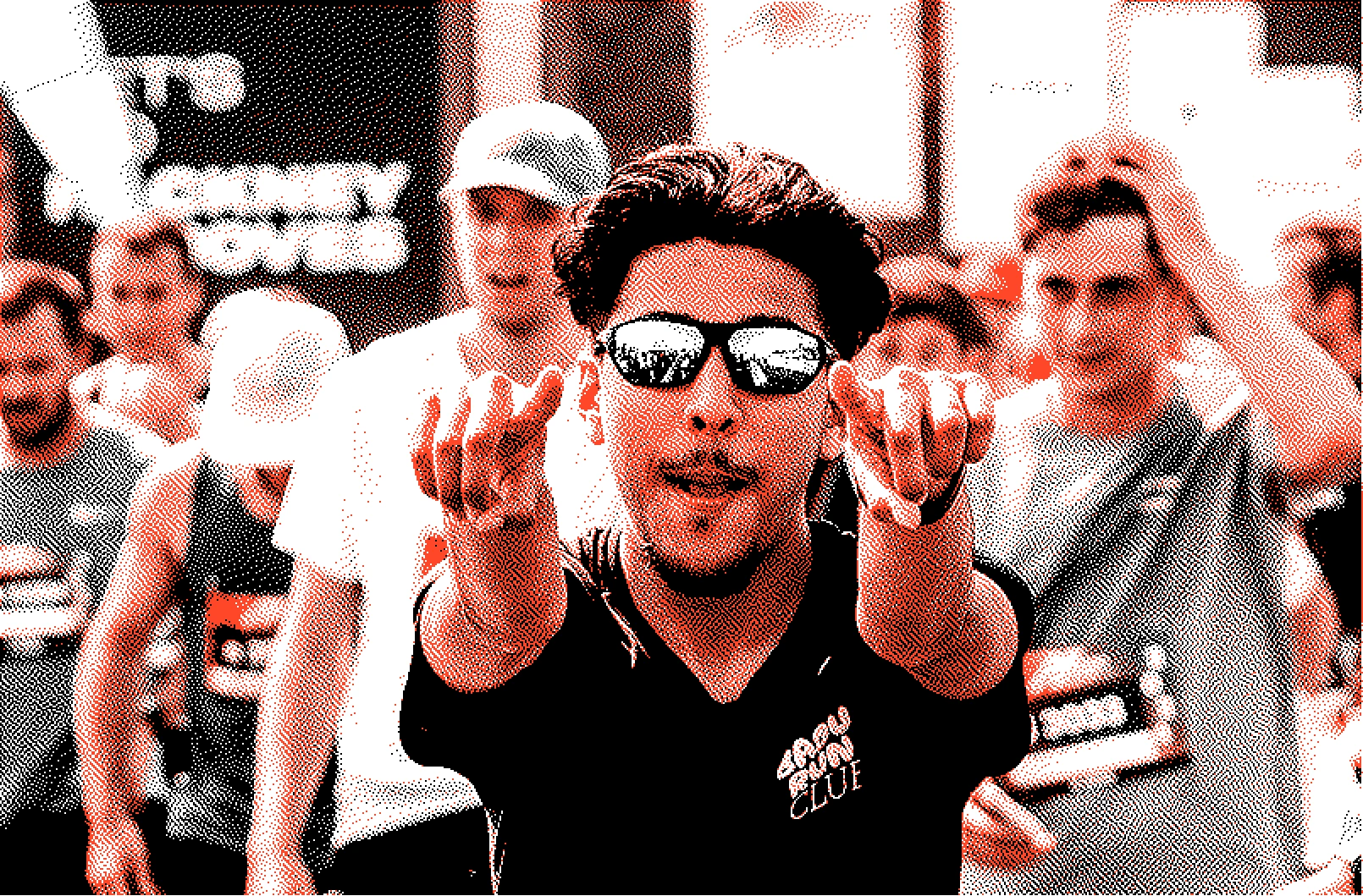 A man wearing sunglasses and a black cap-sleeve shirt points towards the camera with both hands in a crowd at Hackney Moves.