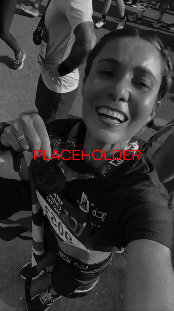 Smiling female runner holding a medal and walking stick, wearing a race bib and sportswear at the London Marathon.