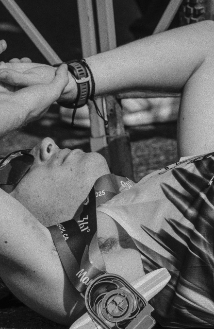 Close-up of a person lying down with arms over head, wearing sunglasses and a medal around the neck.