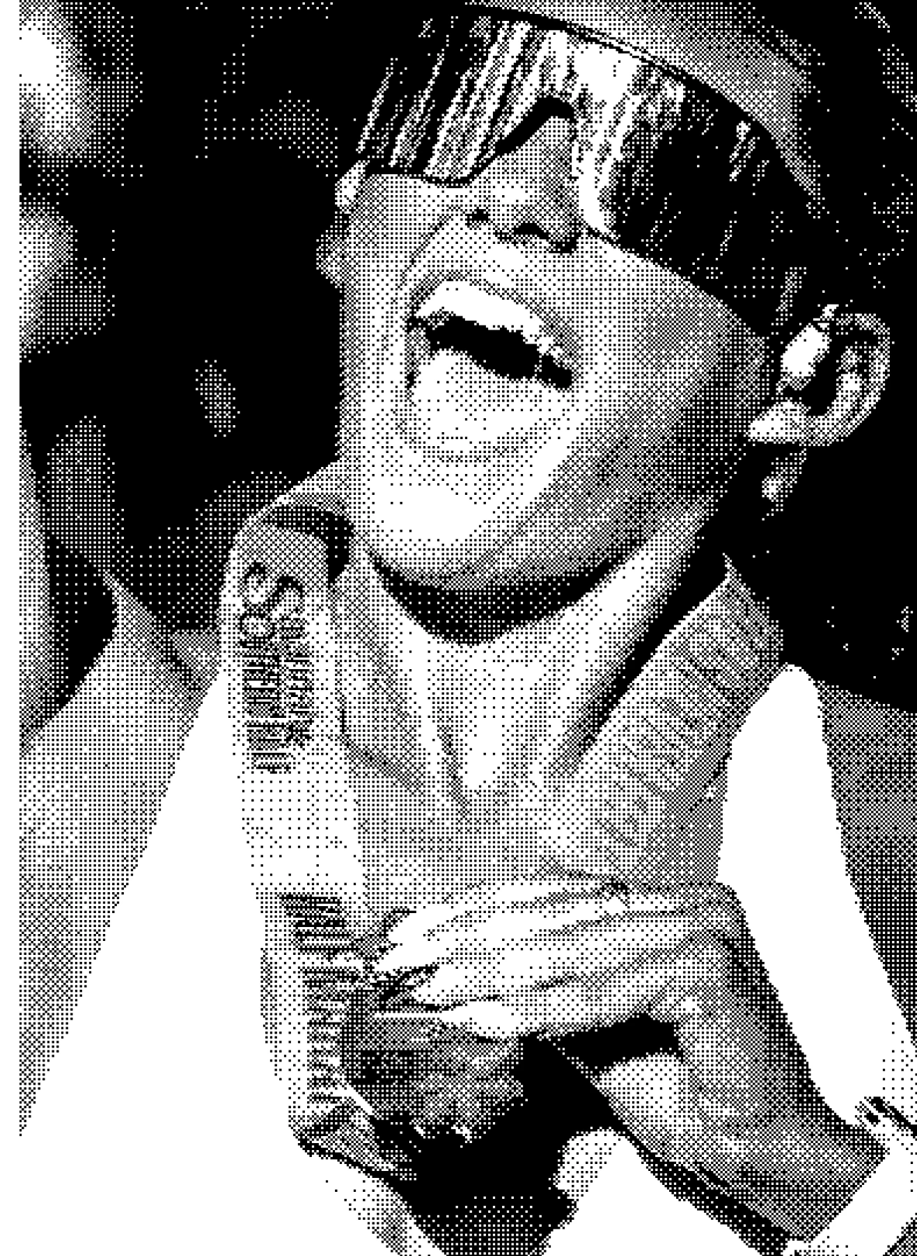 Person smiling widely wearing large reflective sunglasses, a light-colored beanie, and a sleeveless top, holding a necklace.