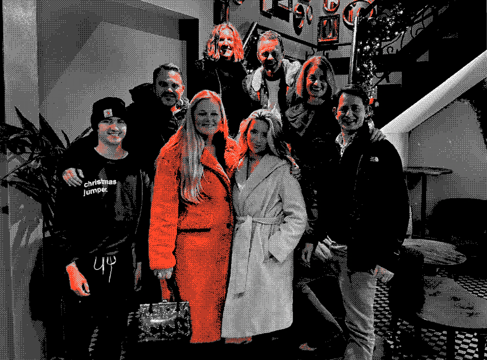 Group of eight people smiling indoors, some wearing coats, posing in front of a staircase and wall decor.