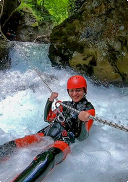 Thrilled woman rappelling down Hrčavka canyon waterfall on rope, guided canyoning tour Bosnia