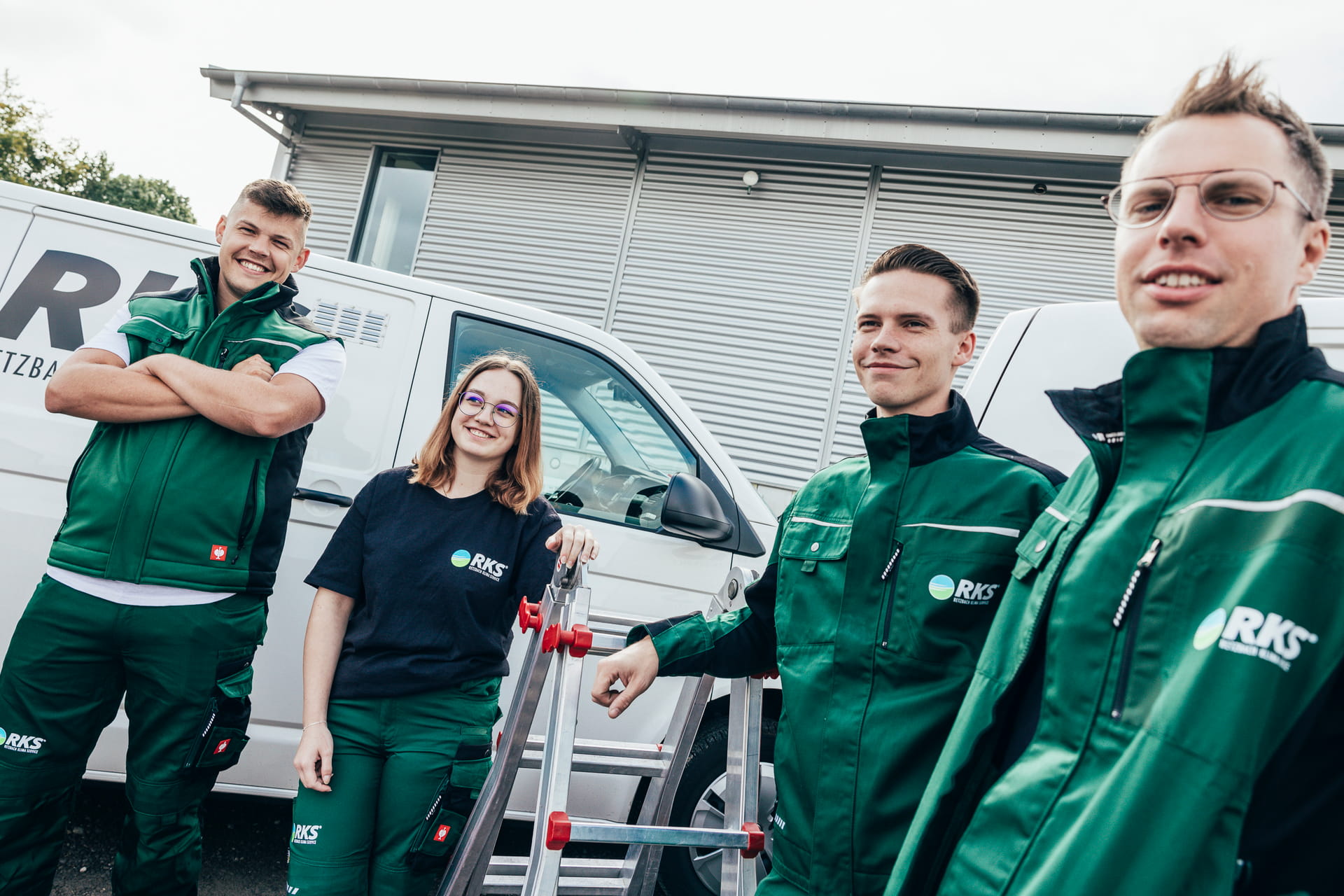 Vier Mitarbeiter der RKS stehen mit Werkzeug und Leiter vor zwei Firmenfahrzeugen