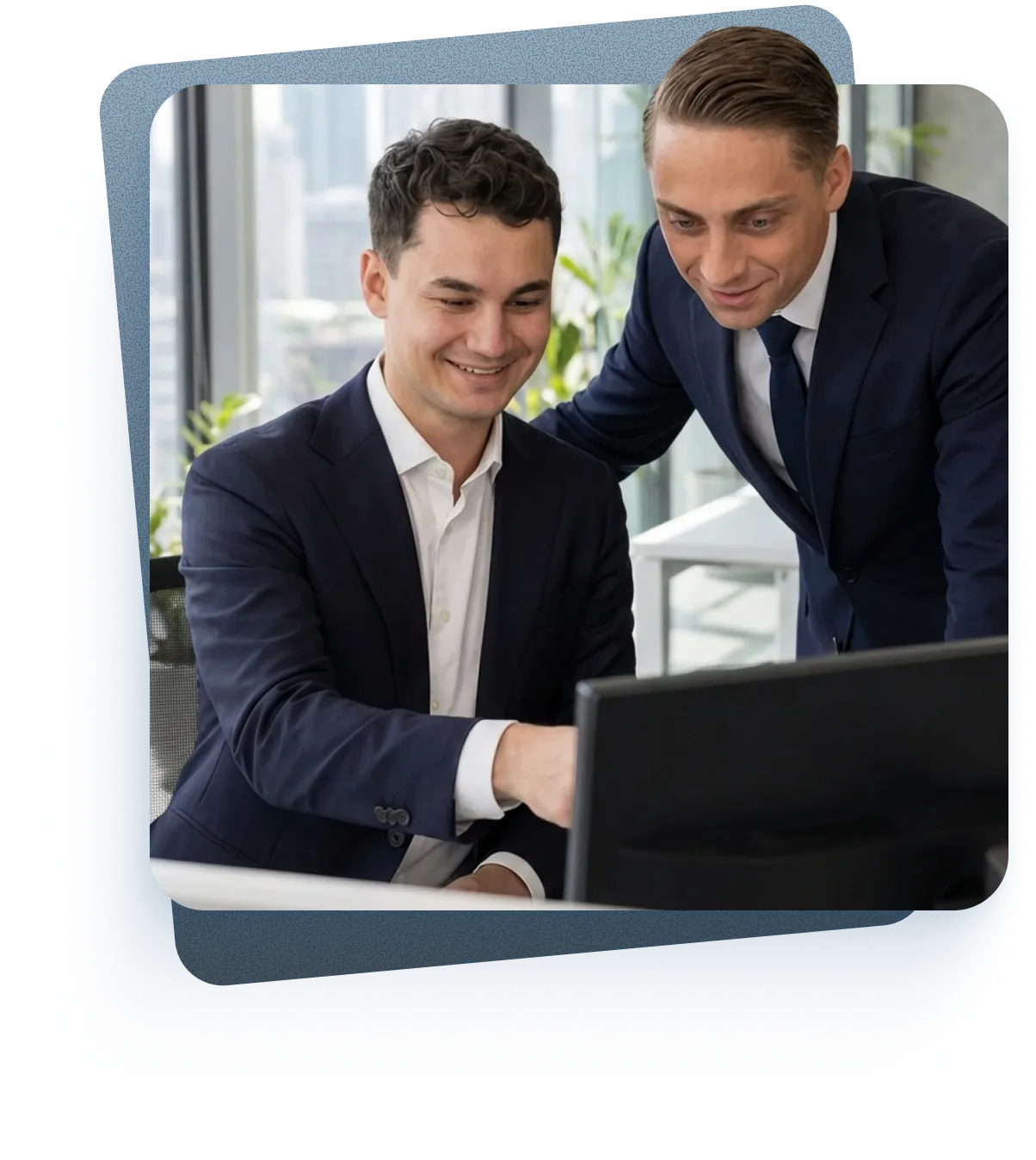 Zwei Geschäftsleute in Anzügen arbeiten gemeinsam an einem Computer in einem modernen Büro.