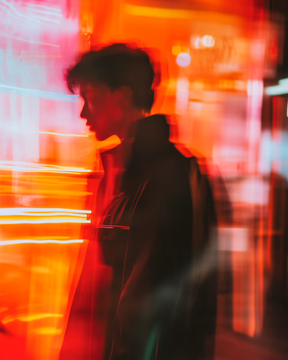Blurred silhouette of a person against vibrant red and orange neon lights.