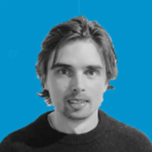 Young man with medium-length brown hair wearing a black sweater against a blue background.