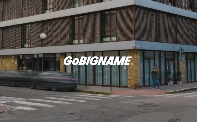 Corner view of a modern building with large windows and stone accents, a blurred car passing by, and a person walking on the sidewalk.