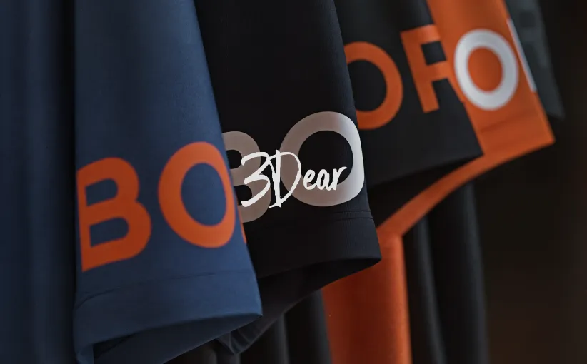 Close-up of hanging shirts with bold orange and white text, showing partial letters on dark fabric.