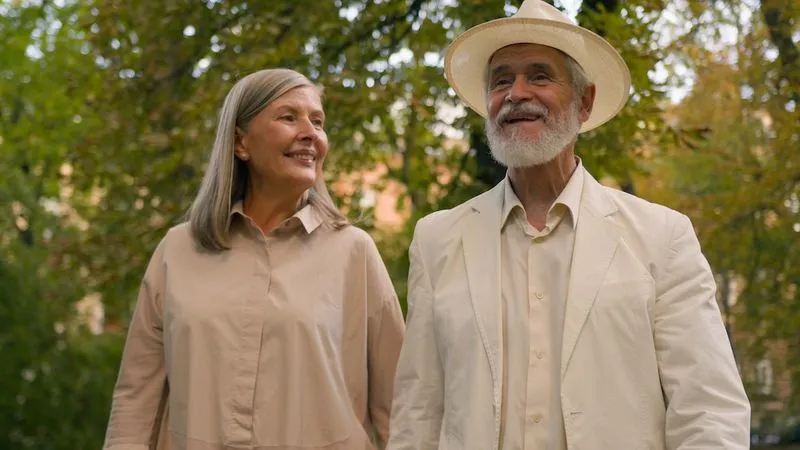 Smiling elderly couple in neutral-toned clothing outdoors among trees